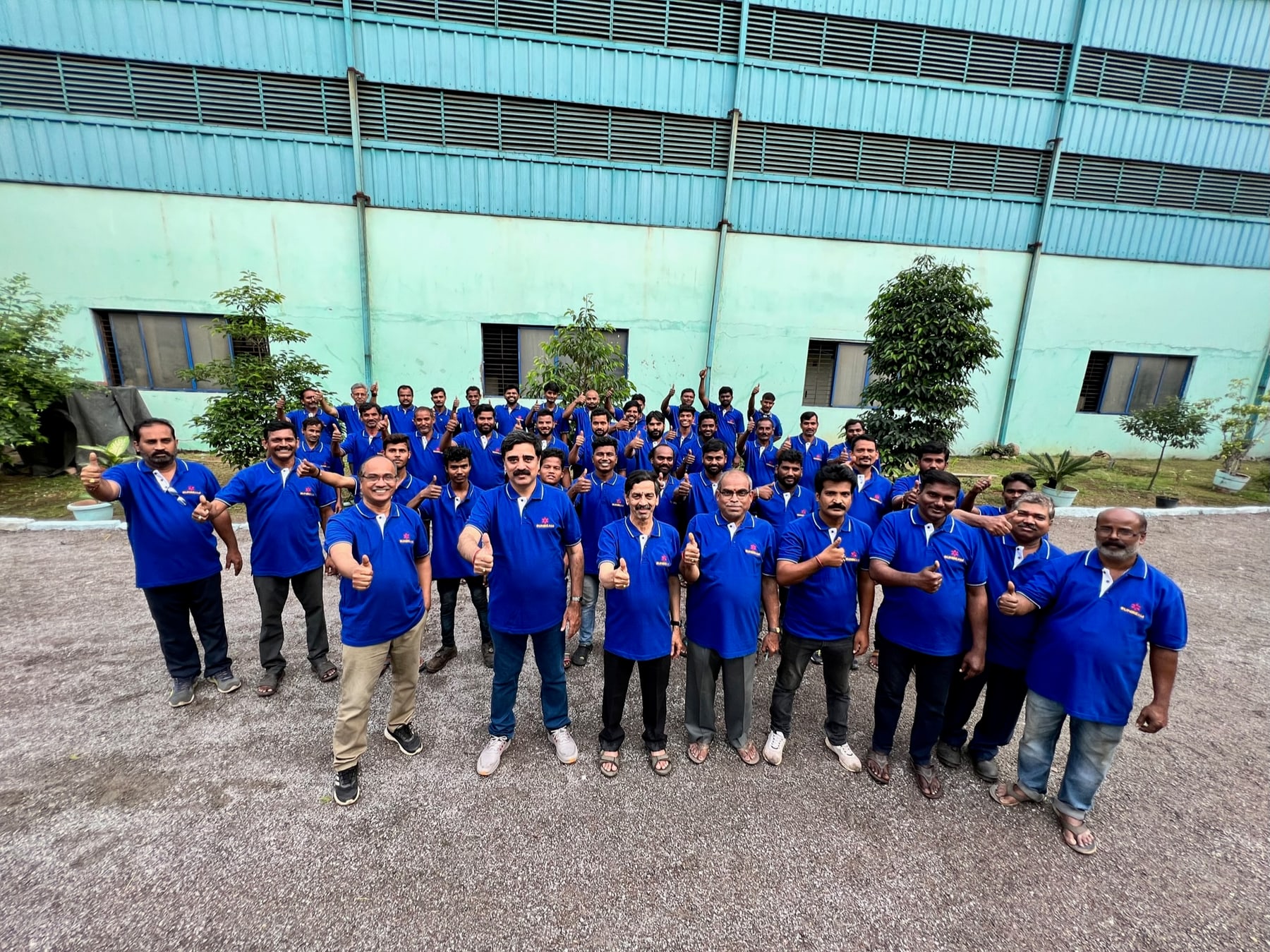 The Sunbeam manufacturing and engineering team, smiling and giving thumbs up in front of the factory